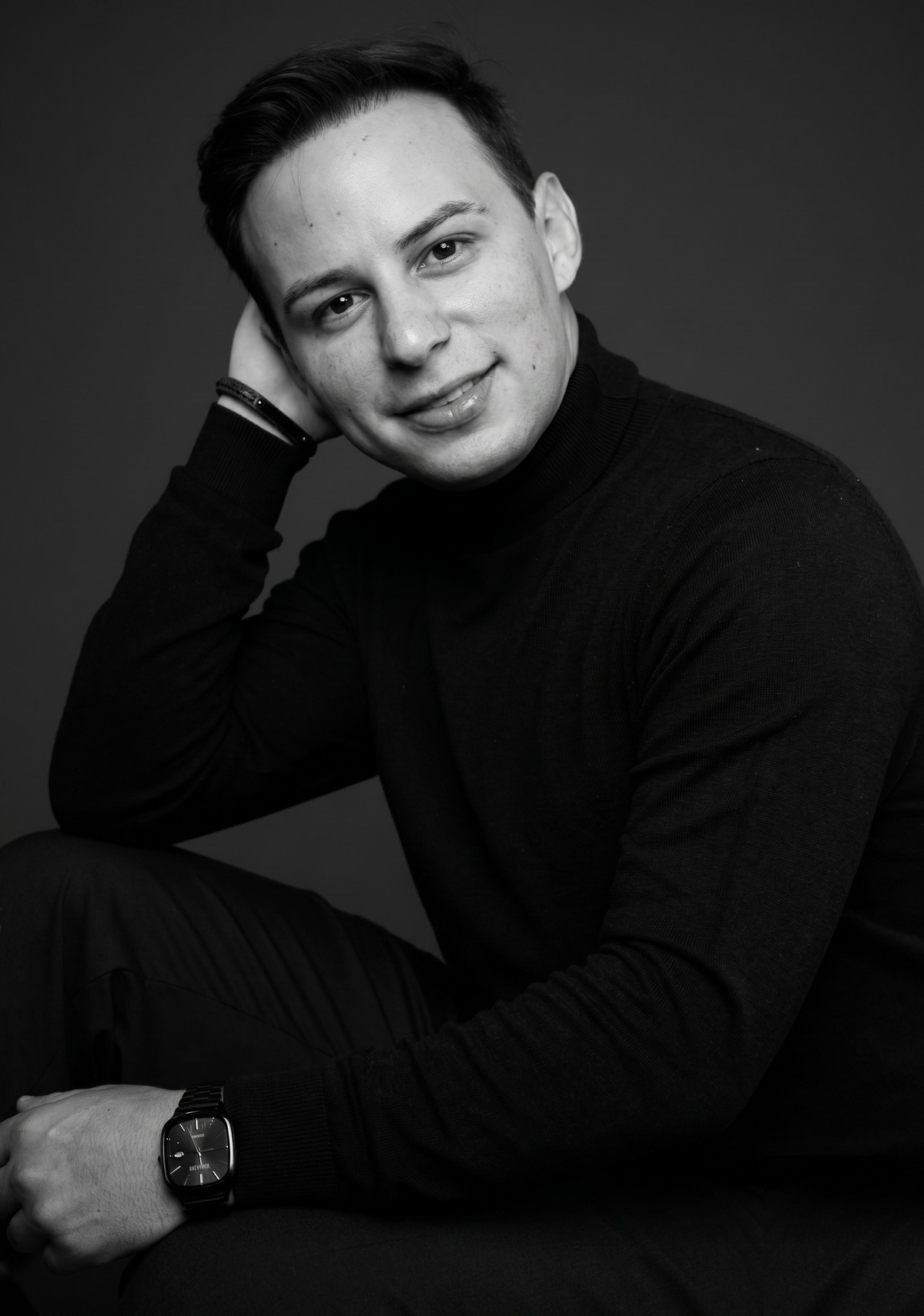 Dr. Lucas Moura em retrato editorial em preto e branco, mão apoiada no rosto, expressão serena e contida.